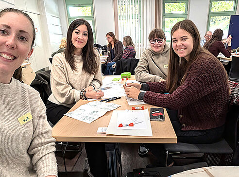 Lehrerinnen und Schülerin lächerln in die Kamera