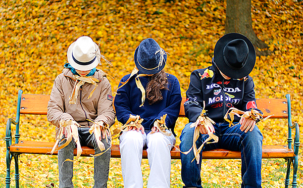 drei Vogelscheuchen auf einer Parkbank vor gelben Laub