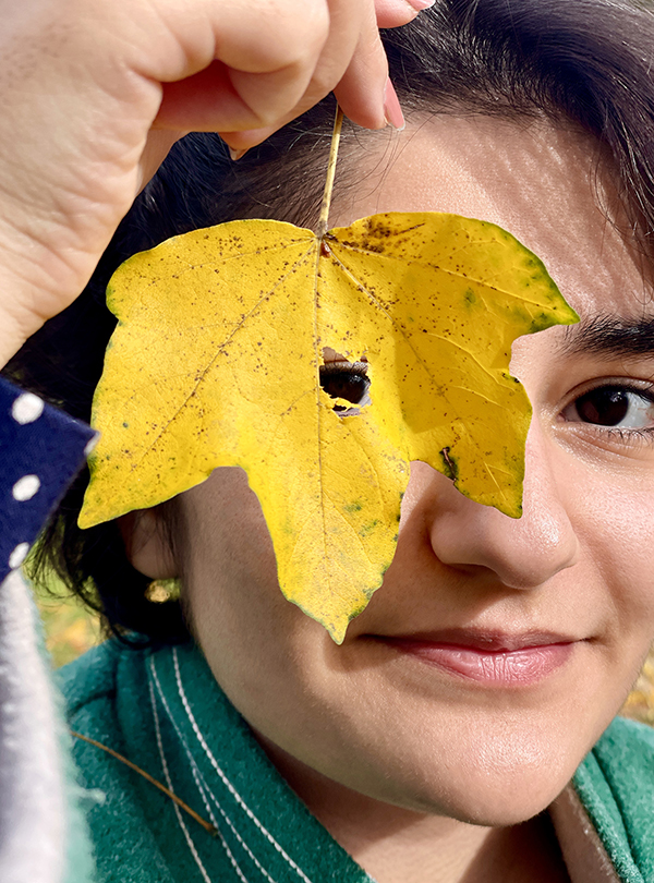 Schülerin schaut durch ein Loch in gelben Ahornblatt