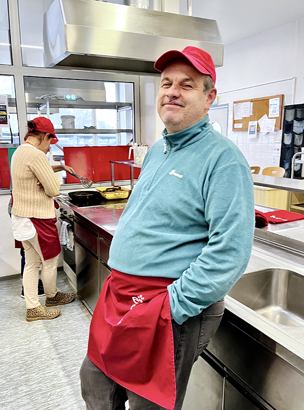 Mann mit roter Kochschürze steht entspannt vor der Abwasch