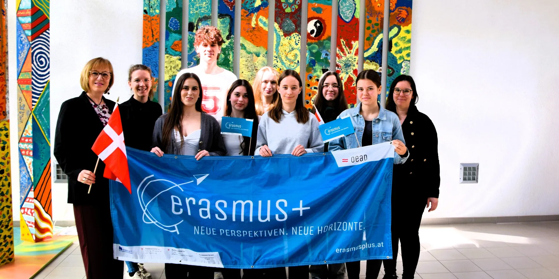 Schülerinnen und Lehrerinnen mit dem Erasmus+-Banner vor der bemalten Wand der ecole güssing