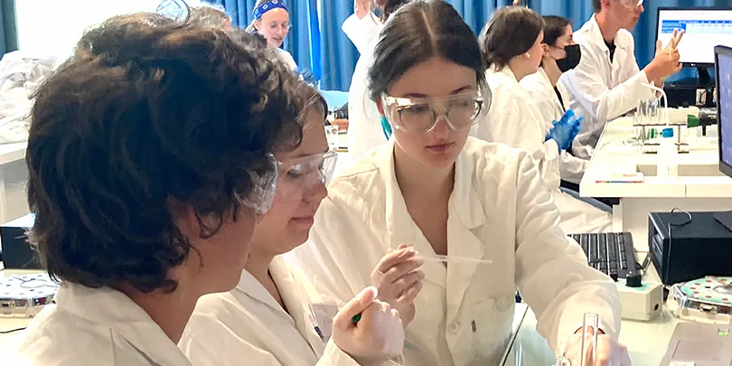 Schülerinnen im Labormantel untersuchen eine Probe